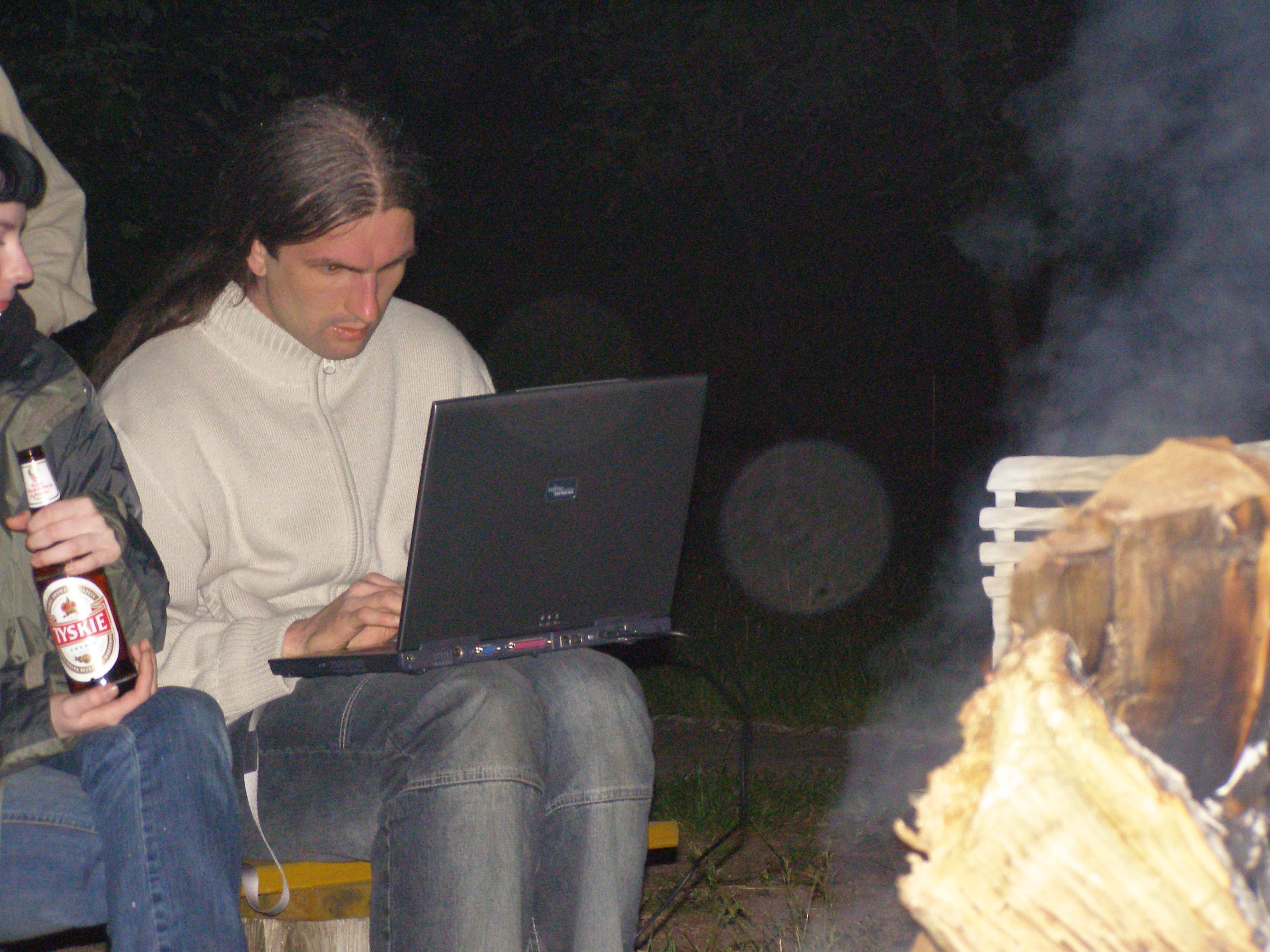 Człowiek siedzący z laptopem przy ognisku